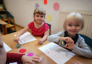 dziewczynki z grupy maluchów robi odciski palców na białych kartkach papieru